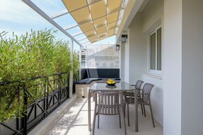 Un balcon doté d’une paroi vitrée, une table avec des chaises et un barbecue noir.