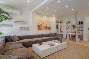 A modern living room with a sectional sofa, a coffee table, and a dining area with a bench. - Sunny Central Retreat with Private Plunge Pool (Athina)