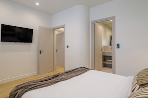 A bedroom with a bed, a TV mounted on the wall, and a door leading to a bathroom. - Sunny Central Retreat with Private Plunge Pool (Athina)