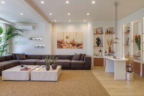 A modern living room with a sectional sofa, two coffee tables, a wall-mounted artwork, and built-in shelves with decorative items. - Sunny Central Retreat with Private Plunge Pool (Athina)