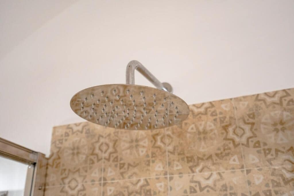 A showerhead with a curved design, mounted on a wall with patterned tiles.