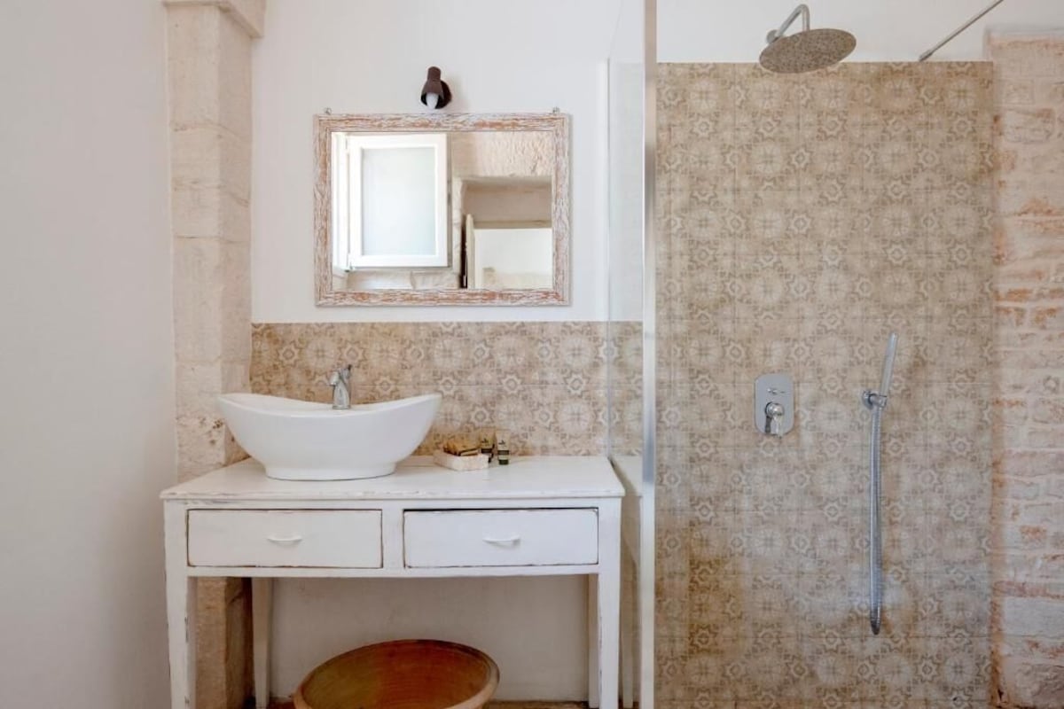Un baño con lavamanos blanco, espejo, ducha y azulejos estampados.