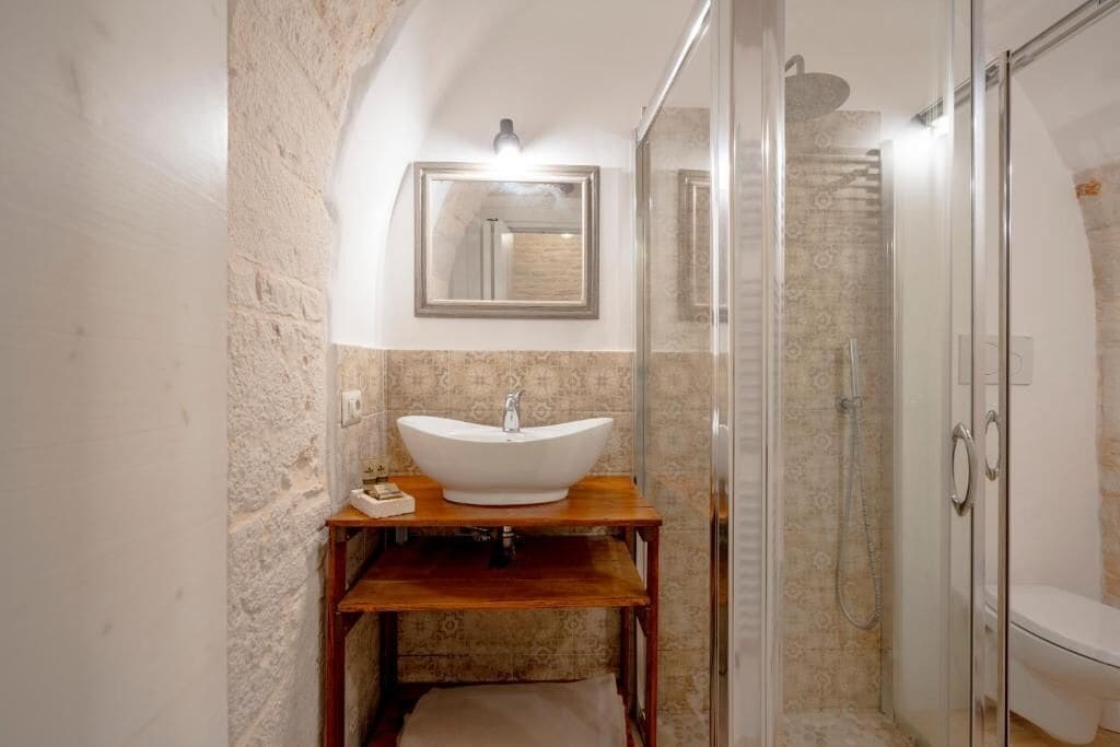 A bathroom with a freestanding sink, a mirror, a shower enclosure, and a toilet.