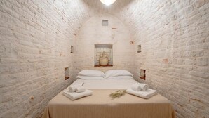 Een smalle kamer met witte bakstenen muren, een bed, handdoeken en een klein raam.