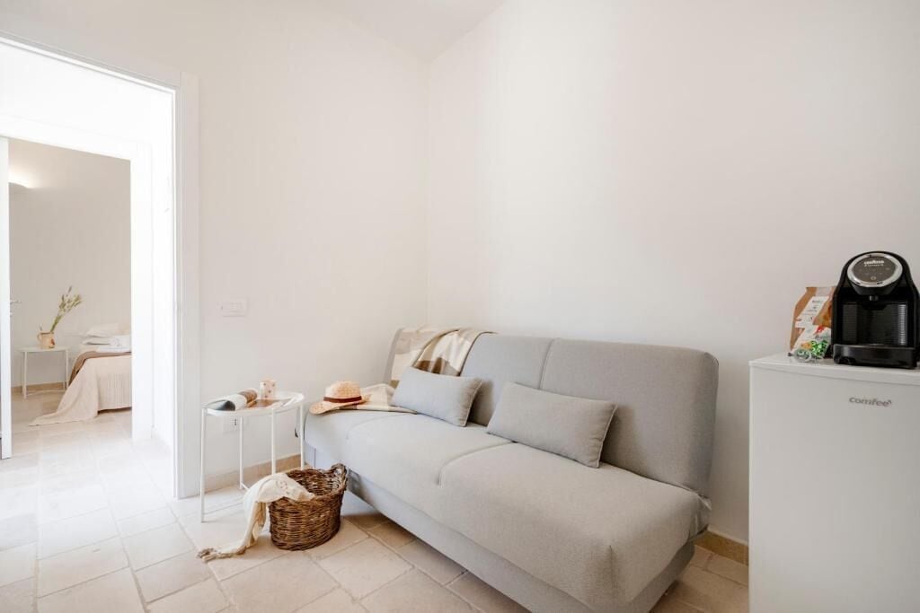 Ett minimalistiskt vardagsrum med en soffa, ett litet sidobord, en korg och en kaffemaskin.