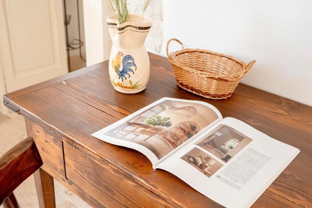 A wooden table with a magazine, a ceramic rooster vase, and a wicker basket.