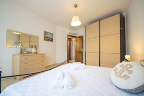 A bedroom with a bed, a dresser, a mirror, a painting, and a door leading to another room. - Casa delle Sorgenti 1 (Torpè)