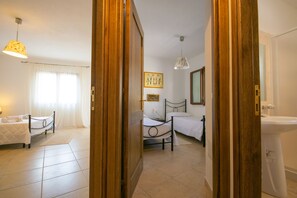 Un dormitorio con dos camas, una mesita de noche, una lámpara, una ventana con cortinas y un baño con lavabo y espejo.