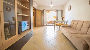 Ein Wohnzimmer mit einer Couch, einem Fernseher, Holzkästen und einem Essbereich mit Stühlen und einem Tisch.