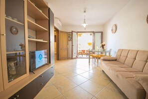 Sala de estar com sofá, TV, armários de madeira e um espaço de jantar com cadeiras e mesa.
