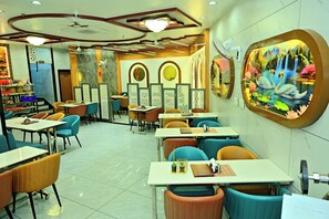Un restaurant doté de nombreuses tables et chaises, d’un ventilateur de plafond et d’œuvres d’art décoratives sur les murs.