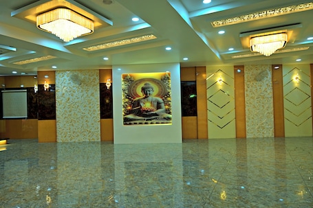 A spacious lobby with a large Buddha statue, chandeliers, patterned walls, and a polished marble floor.. Gehlot Paradise Hotel