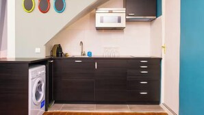 Cocina compacta con muebles oscuros, lavadora integrada, microondas y fregadero.