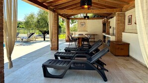Un espace extérieur abrité, aménagé avec des chaises longues, une table et un four en briques.