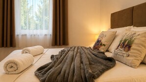 Un lit bien fait, avec une serviette enroulée, une couverture grise et des coussins décoratifs ornés de motifs floraux.