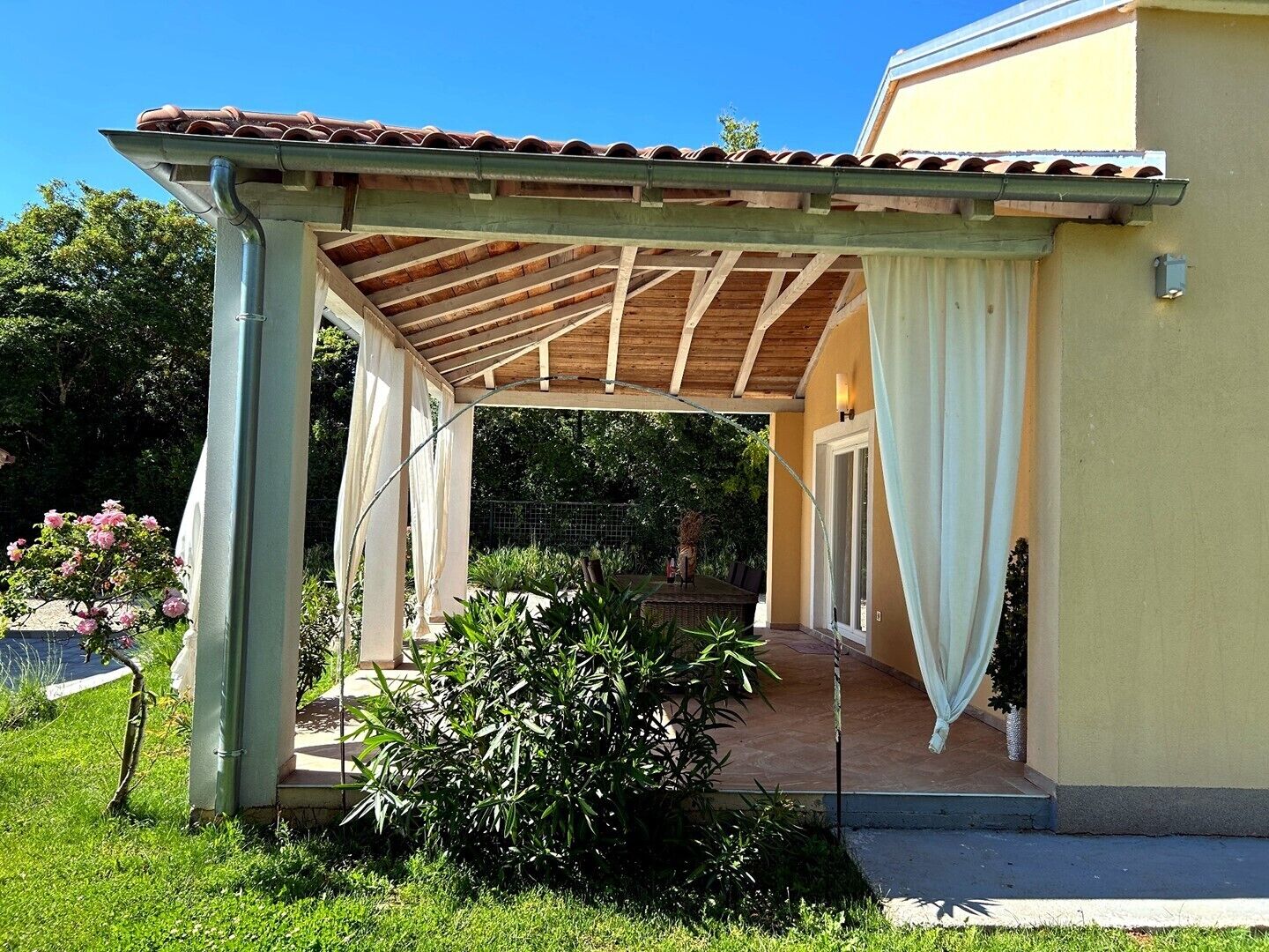 A covered outdoor area with a wooden roof, a concrete floor, and a glass door leading to a building.