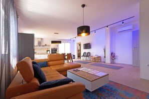 A modern living room with a sofa, coffee table, and a dining area with chairs. - Family house with pool (Divsici)