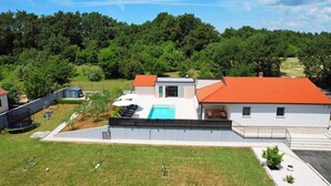 A modern two-story house with a swimming pool, a fenced yard, and a view of a forested area. - Family house with pool (Divsici)