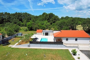 A modern two-story house with a swimming pool, a fenced yard, and a view of a forested area. - Family house with pool (Divsici)