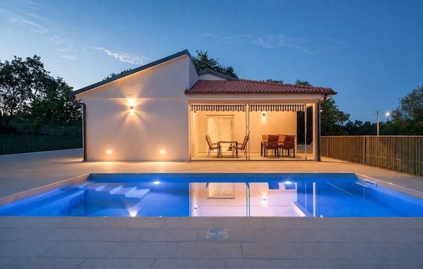 A modern house with a swimming pool, a covered patio with outdoor furniture, and a well-lit entrance. - Family house with pool (Divsici)