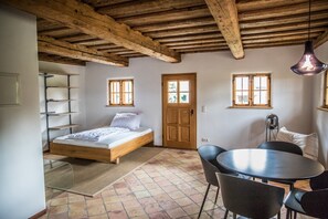 Ein Schlafzimmer mit einem hölzernen Bett, einem kleinen Tisch, zwei Stühlen, einer Tür und zwei Fenstern.