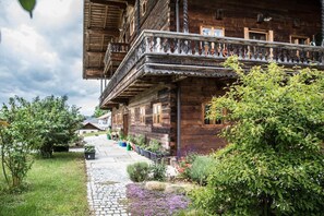 Ein traditionelles Holzhaus mit Balkon, umgeben von einem Garten mit verschiedenen Pflanzen und Blumen.