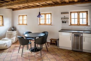 A cozy room with a dining table, chairs, a sofa, a kitchen with a dishwasher, and a wooden ceiling.