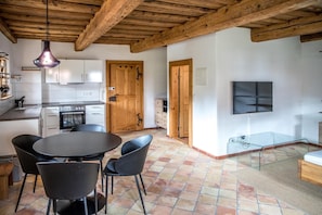 Eine moderne Küche mit weißen Schränken, einem Esstisch mit Stühlen, einer Holzzahlung und einem an der Wand befestigten Fernseher.