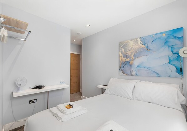 A modern hotel room with a large bed, a bedside table, a wall-mounted artwork, and a wooden door. - Deluxe Double Room with Ensuite - R2 (London)