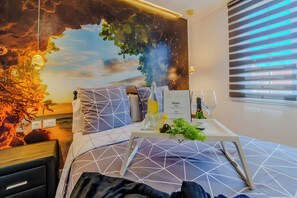 Ein Hotelzimmer mit Bett, Wandgemälde, Fenster mit Jalousien und Tisch mit Tablett.