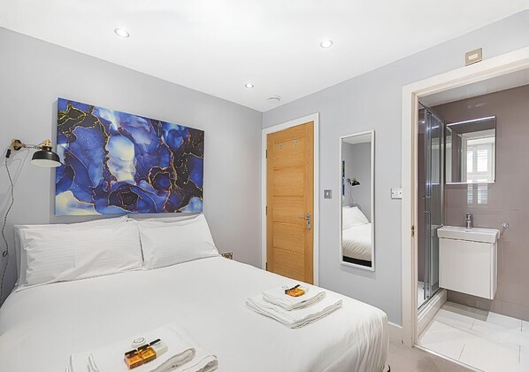 Ein Hotelzimmer mit Bett, einem Gemälde, einer Holztür, einem Badezimmer mit Spiegel und Waschbecken.