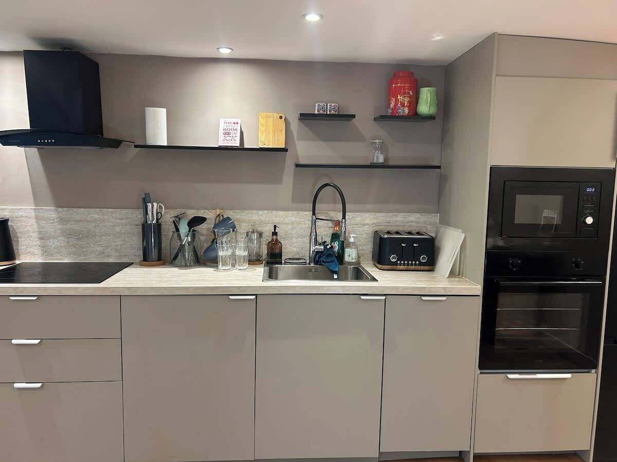A modern kitchen with a built-in oven, a sink, and a countertop with various kitchen items.