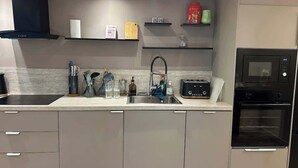 Una cocina moderna con horno integrado, lavamanos y encimera con diversos utensilios de cocina.