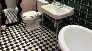 Un baño con piso a cuadros blanco y negro, un inodoro blanco, un lavamanos blanco y una bañera.