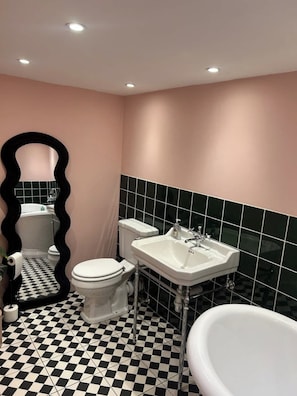 Ein Badezimmer mit einem schwarz-weiß karierten Boden, einer weißen Toilette, einem weißen Waschbecken und einer Badewanne.