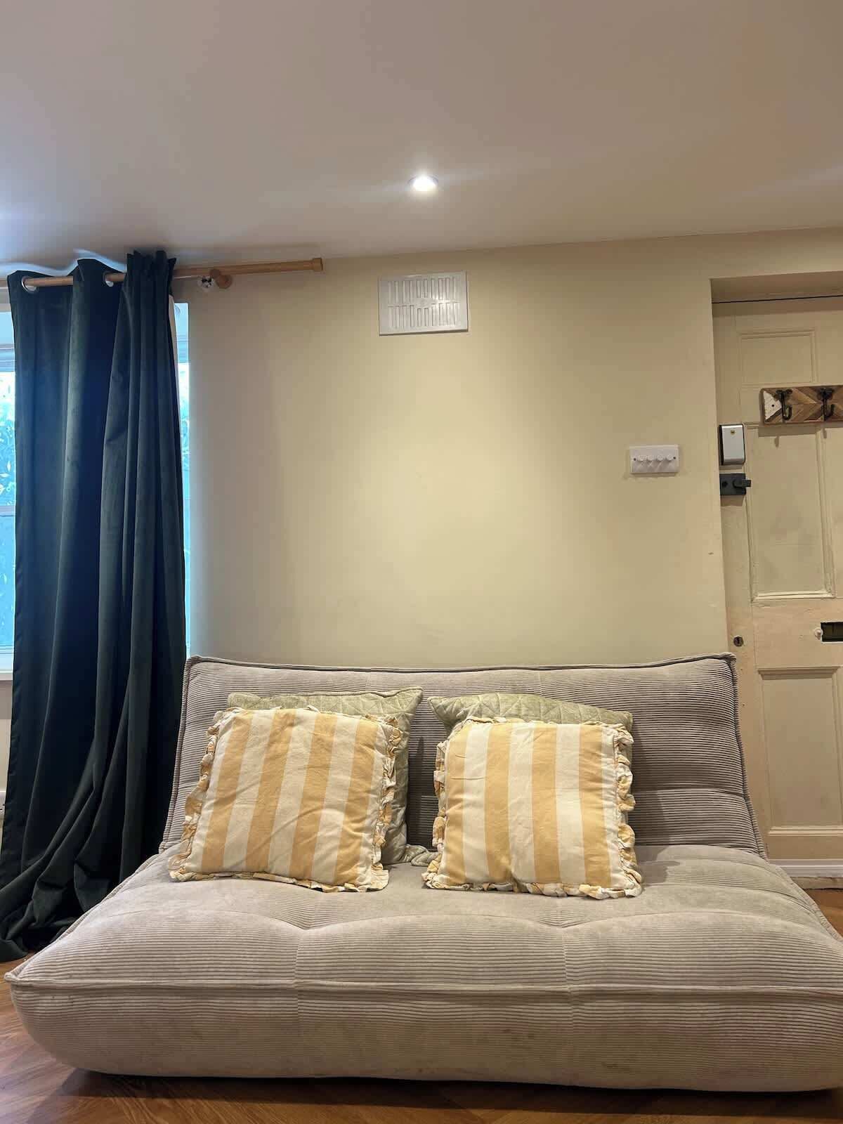 A living room with a sofa, two pillows, a window with curtains, a door, and a light fixture.