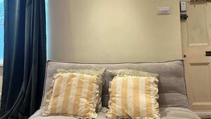 Una sala de estar con un sofá, dos almohadas, una ventana con cortinas, una puerta y una lámpara.