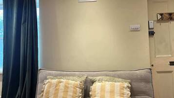 A living room with a sofa, two pillows, a window with curtains, a door, and a light fixture.