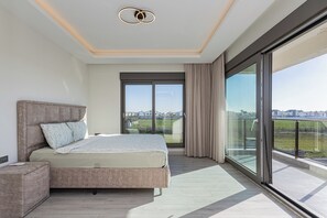 Ein modernes Schlafzimmer mit einem großen Bett, einem Nachttisch, einer Glastür, die auf einen Balkon führt, und Blick auf die Stadt.