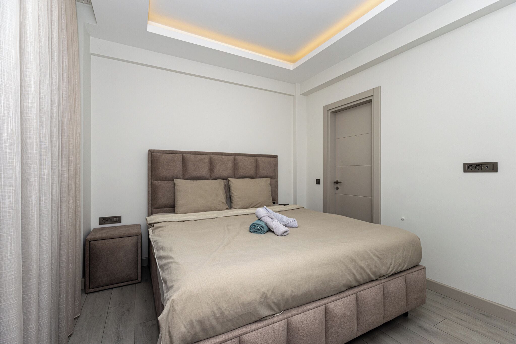 A modern bedroom with a large bed, a bedside table, a wardrobe, and a ceiling light fixture.