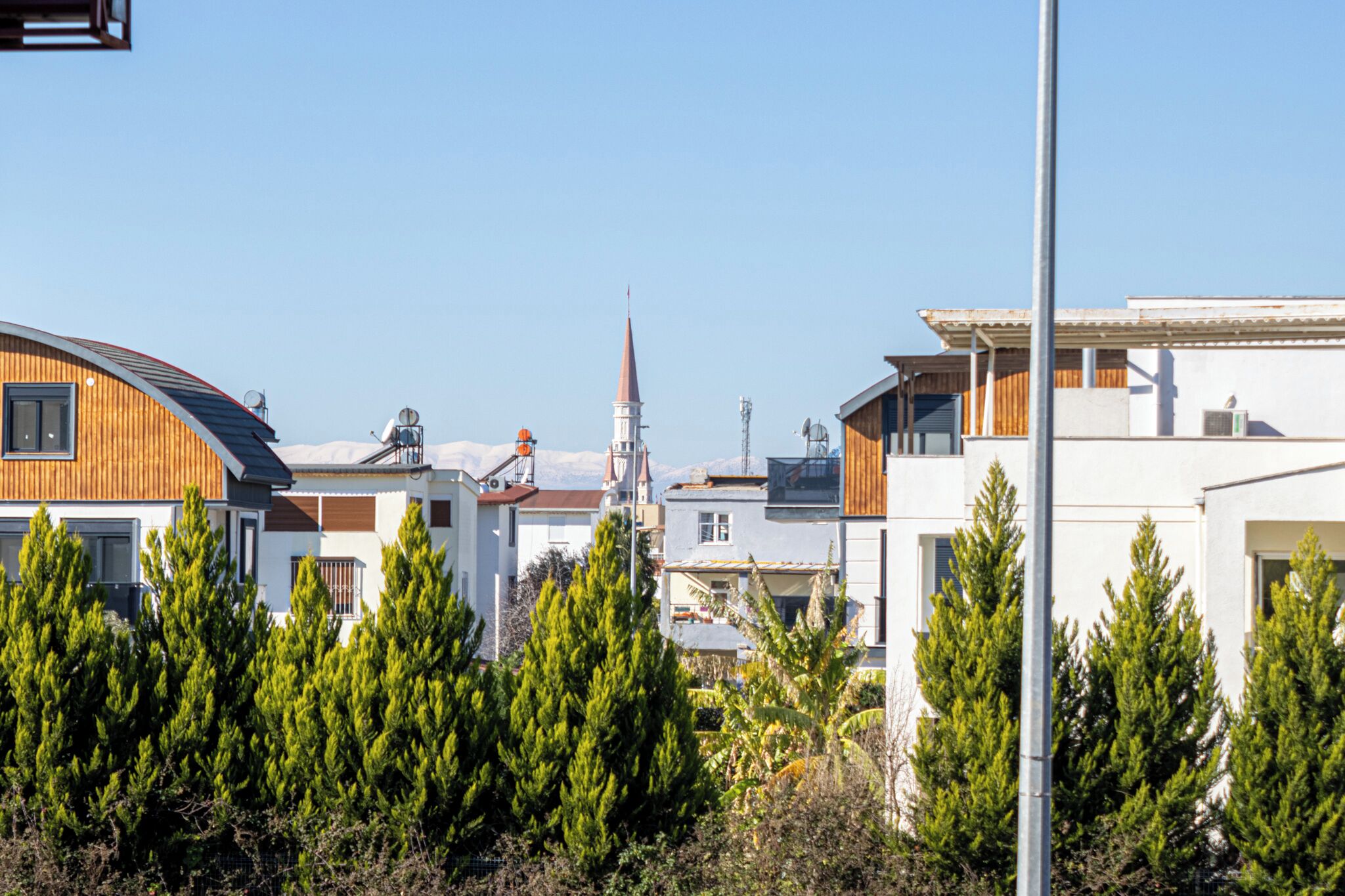 Ett bostadsområde med moderna hus, ett kyrktorn och städsegröna träd.