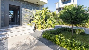 Un edificio moderno con fachada de piedra, un jardín bien cuidado y un cielo despejado.