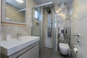 Ein modernes Badezimmer mit einer begehbaren Glasdusche, einem weißen Waschbecken und einer Toilette.