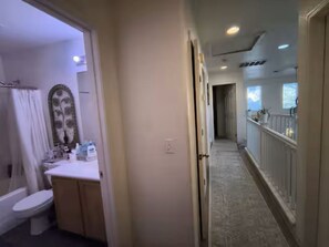 Un pasillo con un baño a la izquierda, una escalera a la derecha y vistas del cielo a través de las ventanas.