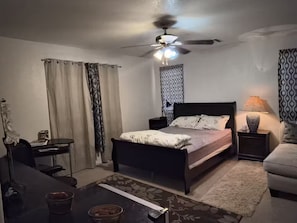 A bedroom with a bed, a desk, a chair, a ceiling fan, and a nightstand with a lamp. - 1-bedroom bed & breakfast in delightful Las Vegas with AC (Las Vegas)