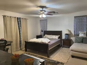 A bedroom with a bed, bedside tables, a desk, a chair, a ceiling fan, and patterned curtains. - 1-bedroom bed & breakfast in delightful Las Vegas with AC (Las Vegas)