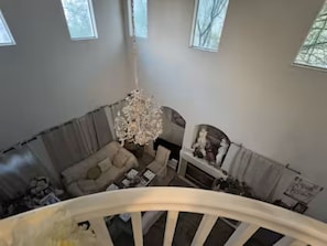 Ein geräumiges Wohnzimmer mit einer Chandelüster, einem Kamin und Blick ins Freie durch große Fenster.