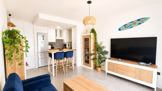 Ett modernt vardagsrum med en soffa, ett soffbord, en TV och en köksdel med ett matbord och stolar.