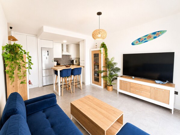 A modern living room with a sofa, coffee table, TV, and a kitchen area with a dining set. - El Mirador del Sol . (Conil de la Frontera)