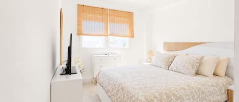 A bedroom with a bed, bedside table, lamp, and a television on a white dresser.